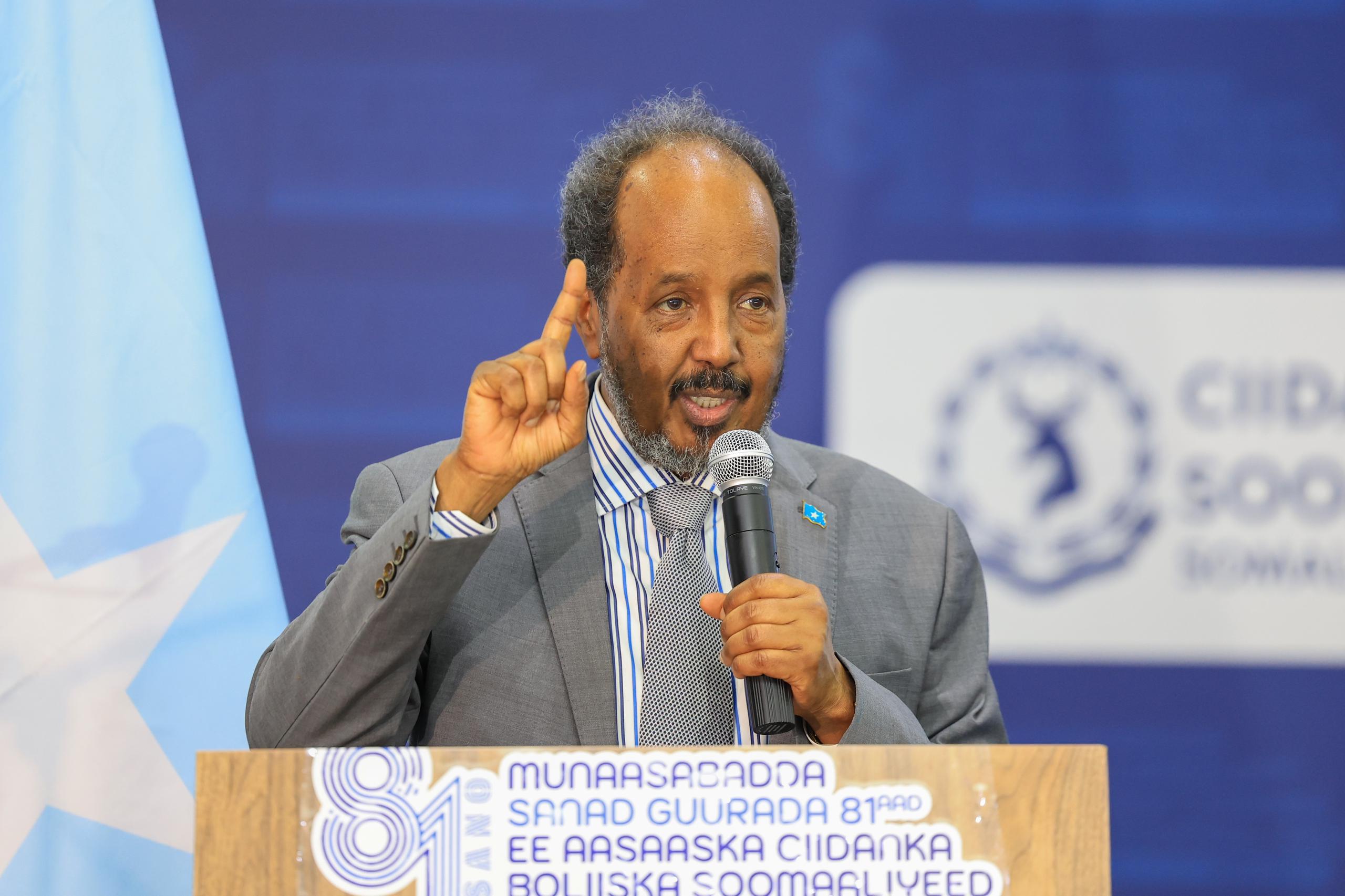 omali President Hassan Sheikh Mohamud stands at a podium, addressing attendees during the 81st-anniversary celebration of the Somali Police Force. The event, held today, is captured in a vibrant image by Dawan TV, showing the President delivering his speech against a backdrop adorned with official emblems and banners.