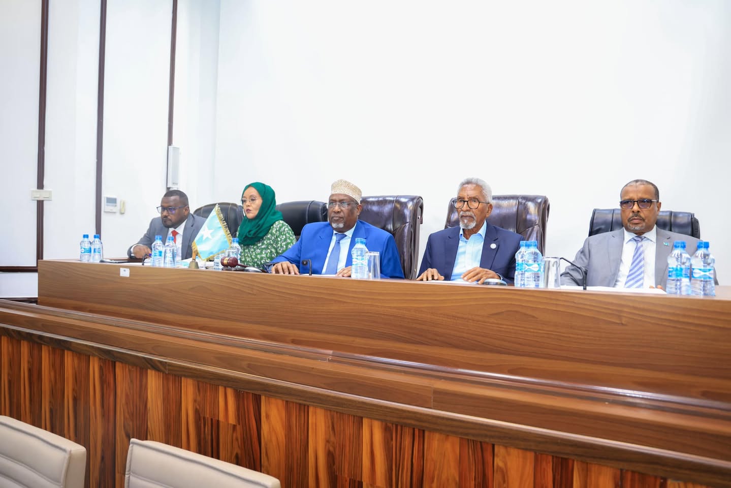 The leadership of Somalia’s two houses of Parliament seated at the front of a parliamentary session. They are dressed in formal attire, with a Somali flag placed on the table.