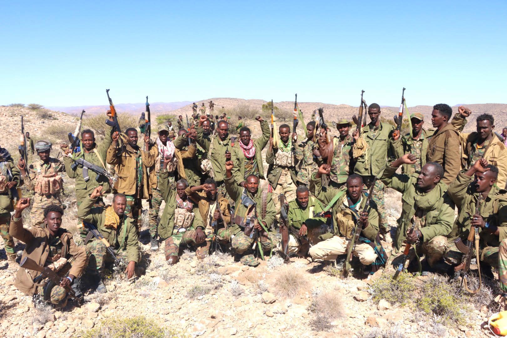 A group of Puntland forces in military uniforms, armed with rifles, raising their weapons and fists in the Cal Miskaad Mountains, a rugged and strategic area in northern Somalia.