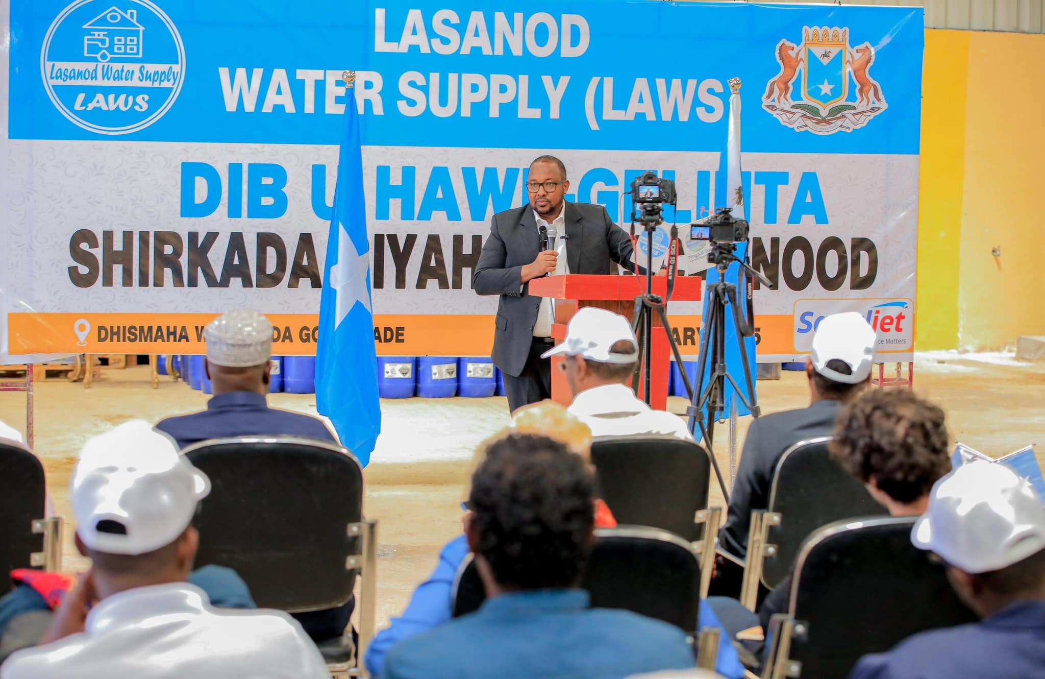 SSC-Khaatumo leader Cabdiqadir Axmed Aw-Ali delivers a speech at the re-launch event of the Lasanod Water Supply (LAWS) company. The Somali flag stands beside him, and a large banner in the background highlights the event’s purpose.