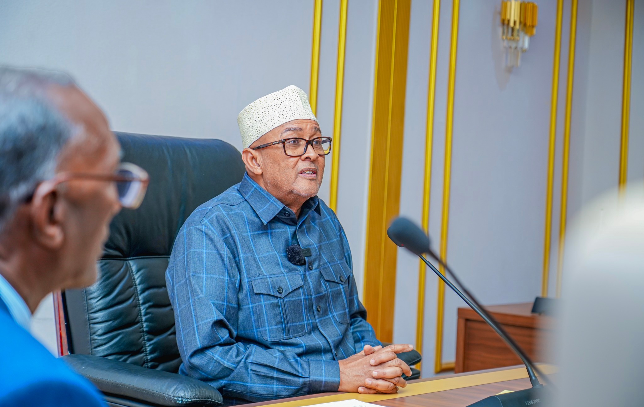 Somaliland President Cabdiraxmaan Maxamed Cabdillaahi (Cirro) speaking at a meeting on February 17, 2025, dressed in a blue plaid shirt and wearing a kufi cap. A microphone is positioned in front of him as he engages with regional governors.