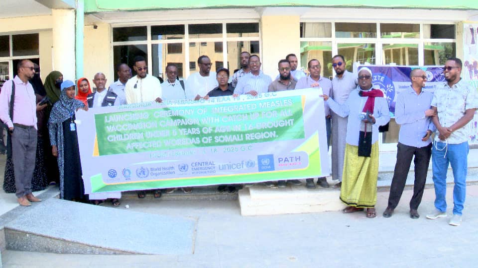 A group of healthcare officials, community leaders, and organization representatives stand in front of a building holding a banner for the launch of an integrated measles vaccination campaign for children under five in drought-affected areas of the Somali region.