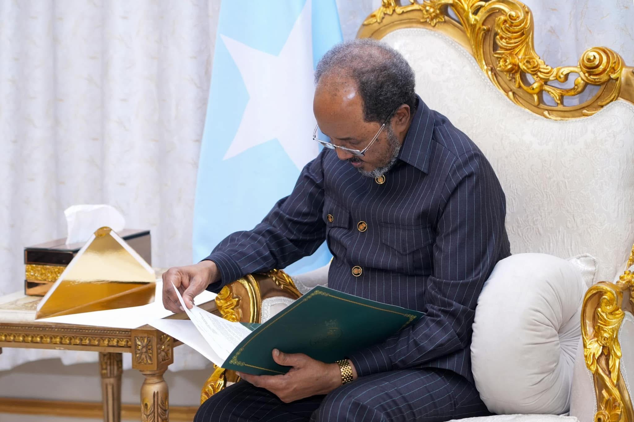 Somali President intently reviewing and signing documents in an ornate office, with the Somali flag in the background.