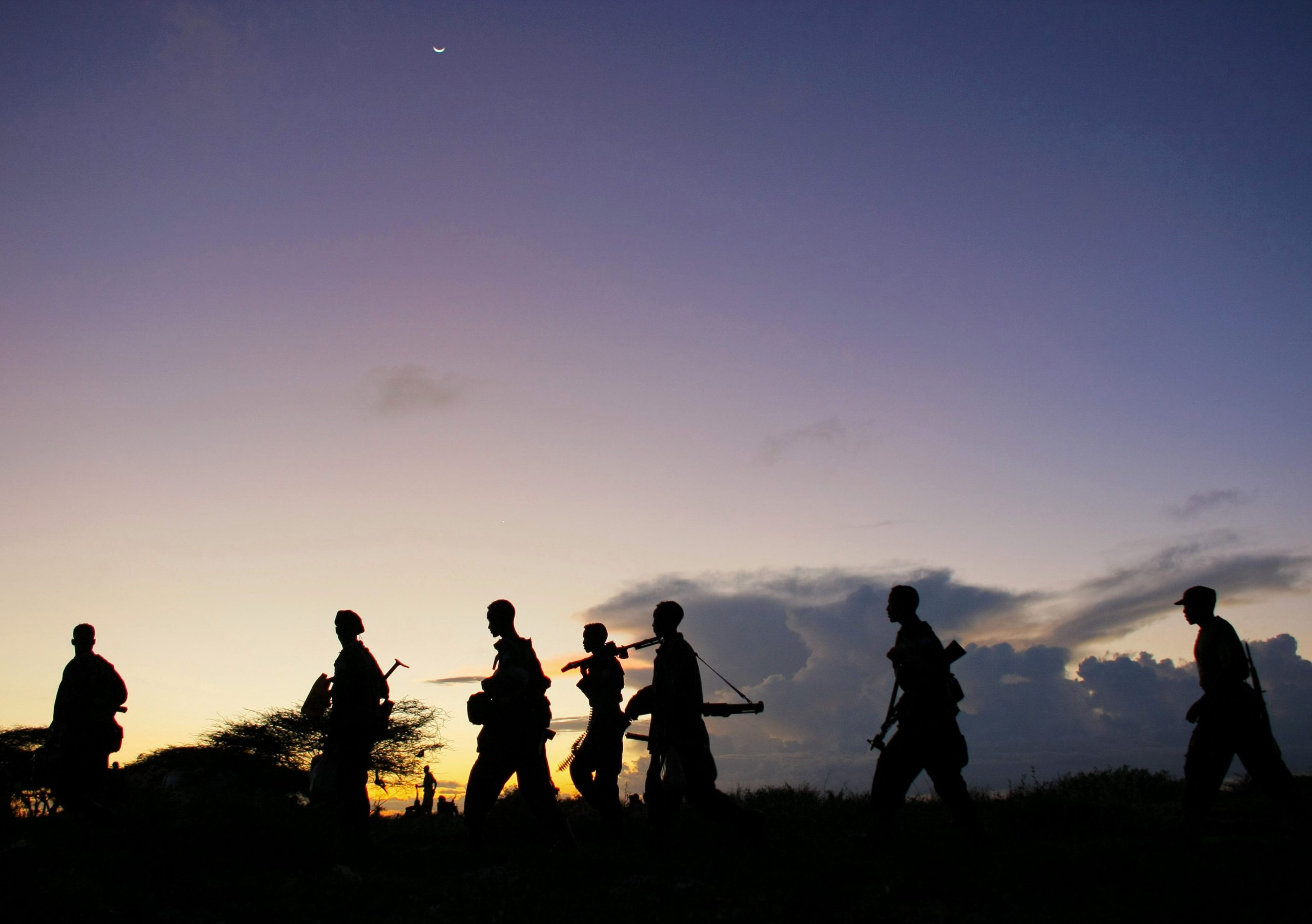 Somali National Army (SNA) soldiers walking at dusk under a rising crescent moon.