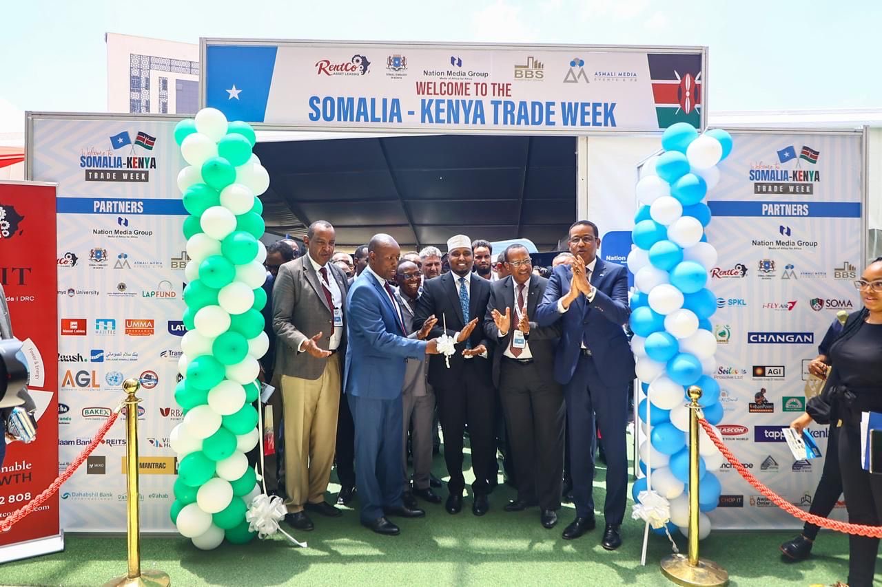 Officials at the ribbon-cutting ceremony of the Somalia-Kenya Trade Week, with a crowd clapping and festive balloons decorating the entrance.