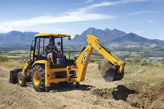 A JCB backhoe loader operating on a construction site, digging into the soil with a scenic mountainous landscape in the background.