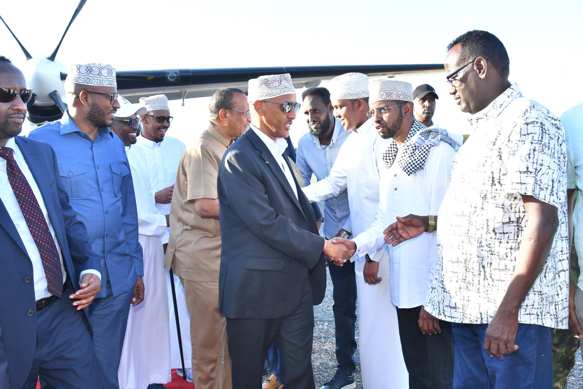 The President of the Somali Regional State shaking hands with officials and community members upon his first visit to Garisa, Kenya, with a small aircraft in the background.