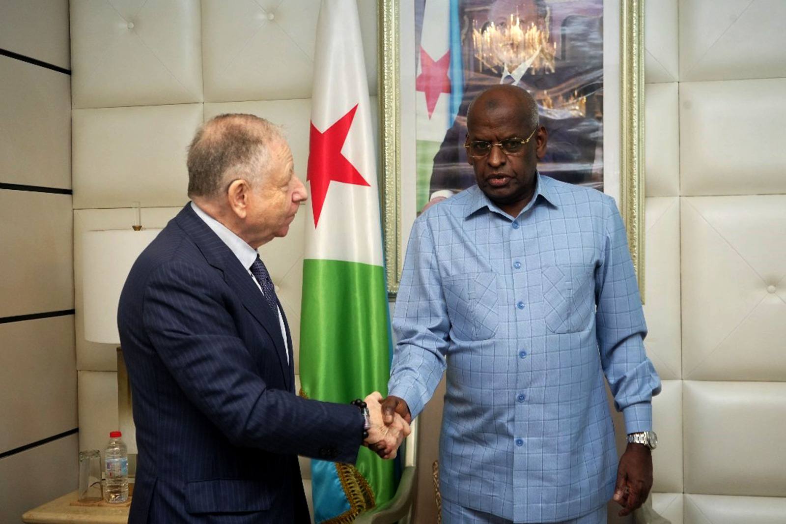 Djibouti government official shakes hands with a United Nations representative amid a backdrop of Djibouti and UN flags.