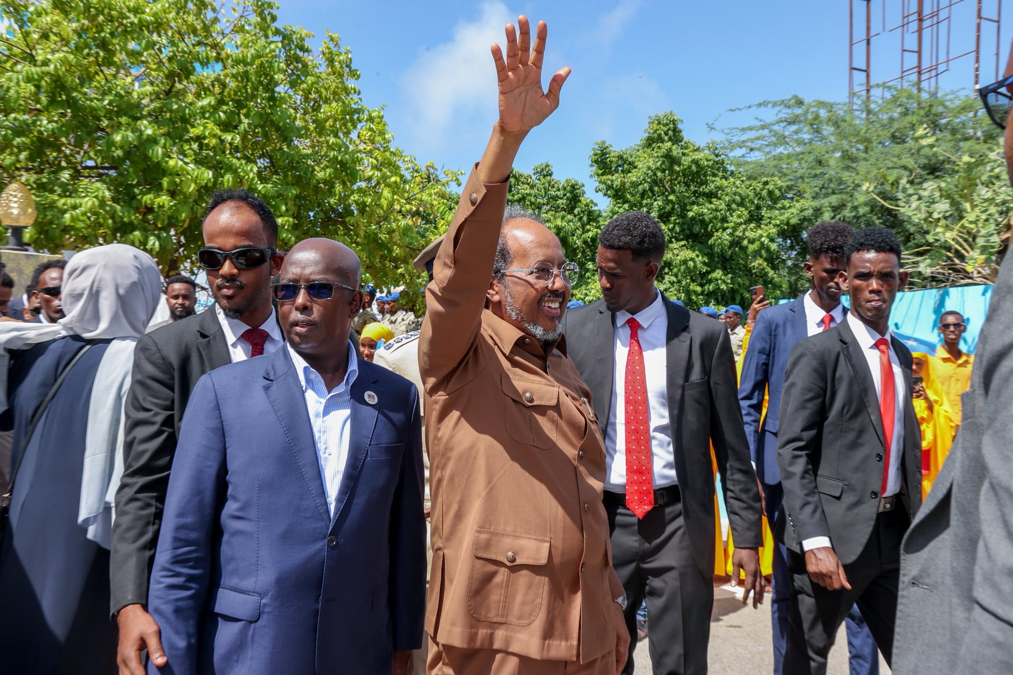 President Hassan Sheikh raising his hand to greet the public while accompanied by his personal security detail.